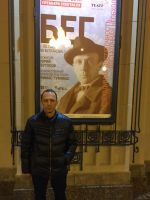Actor of Arlekin Players Theatre in front of a theatre poster with the picture of Mikhail Bulgakov